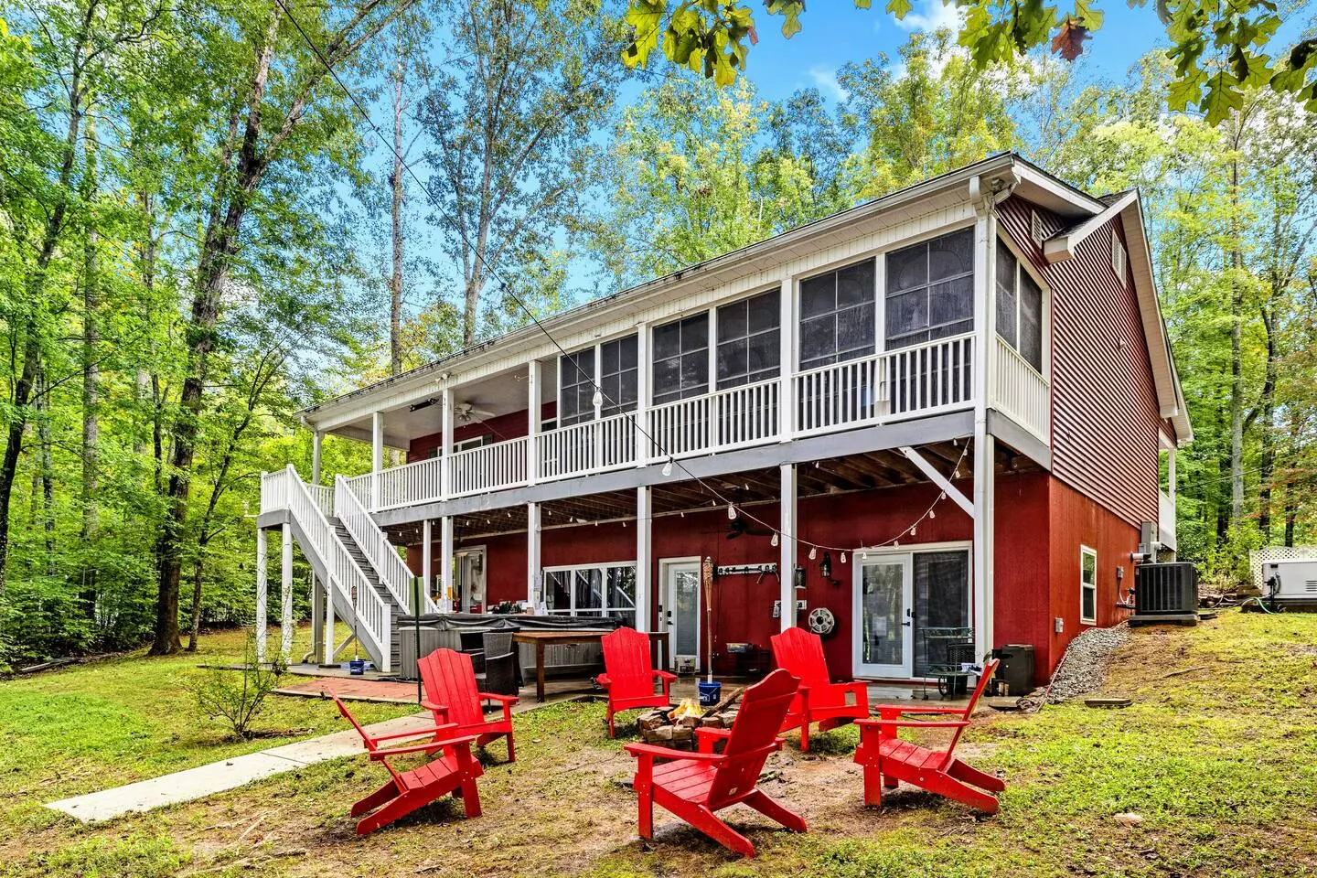 Two-story red lake house with a wraparound screened porch and string-lit lower deck among tall trees