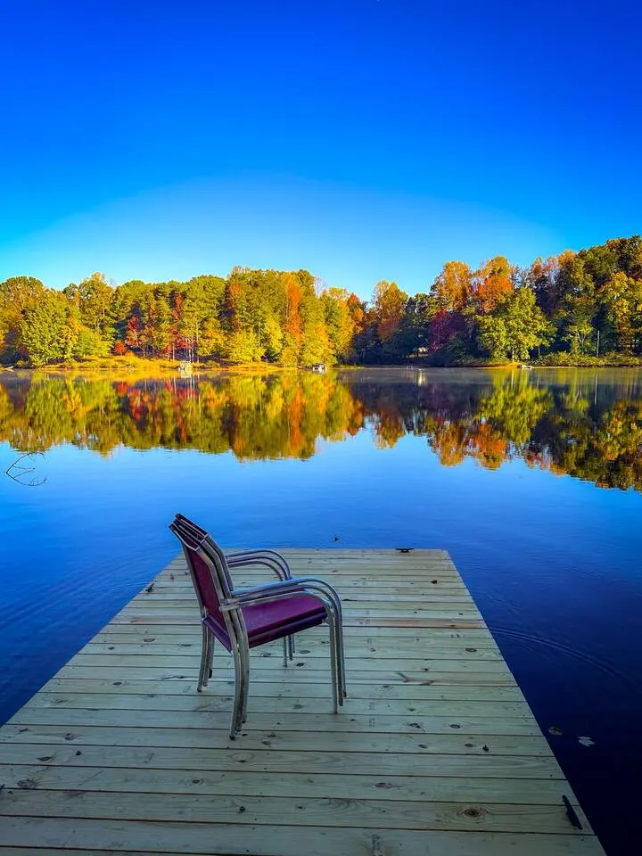 A chair at the end of the private dock facing still water and autumn foliage