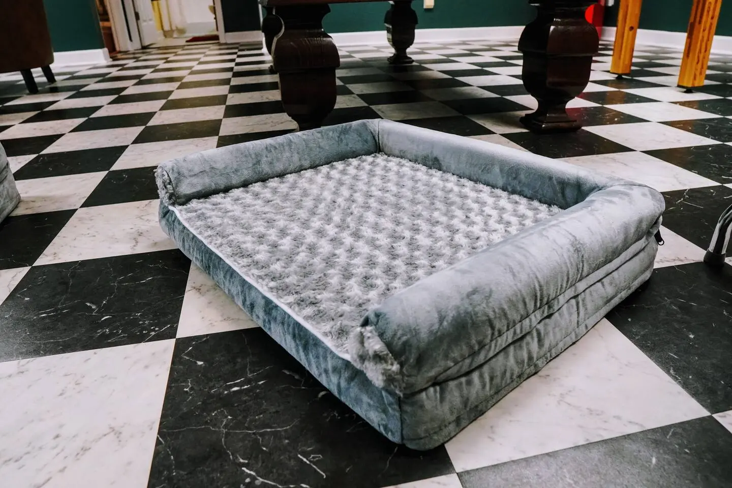 Plush gray dog bed on the checkered game-room floor