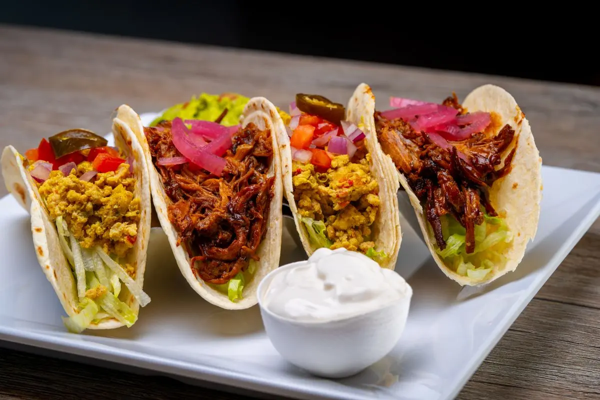 A row of soft tacos with assorted fillings on a white plate